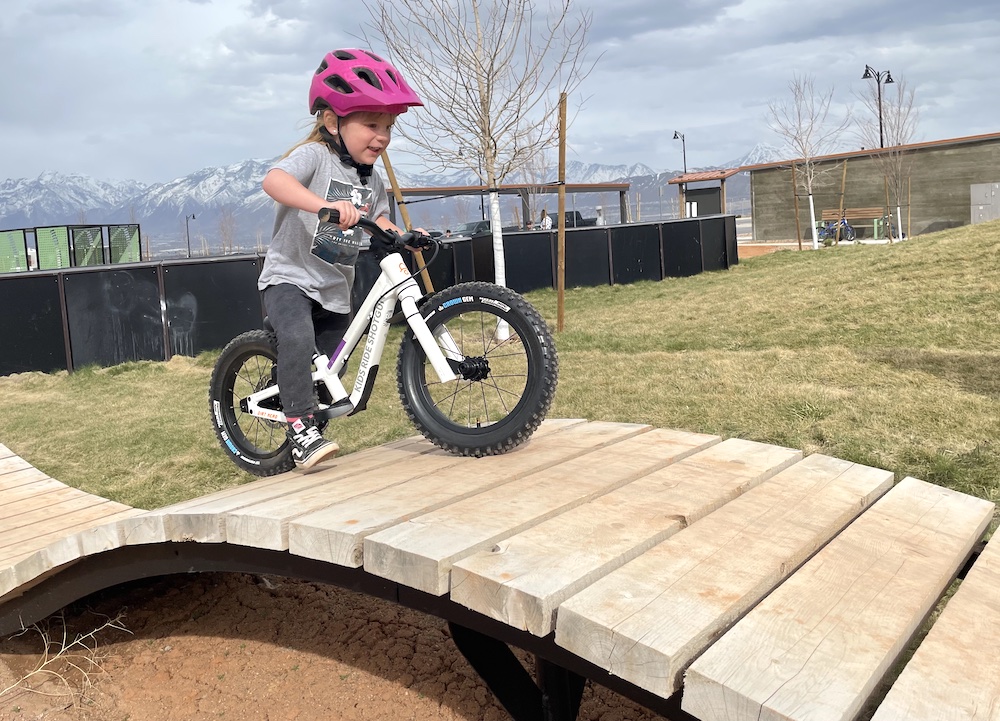 girl rolling over a wood features on her 14" Dirt Hero balance bike