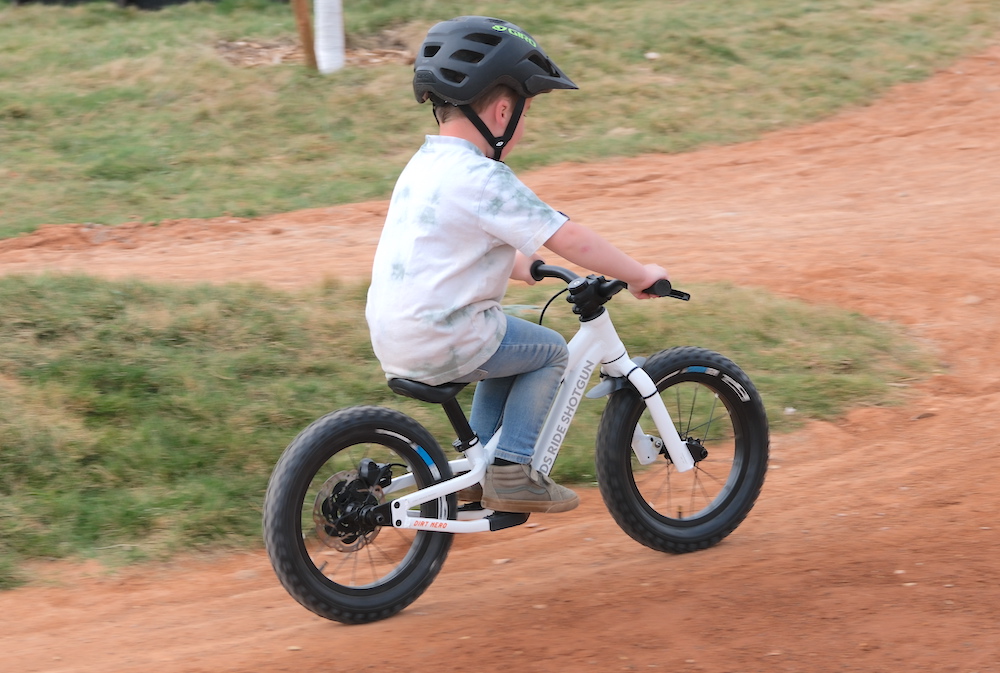 boy sitting down with his legs up on the footrests of his balance bike