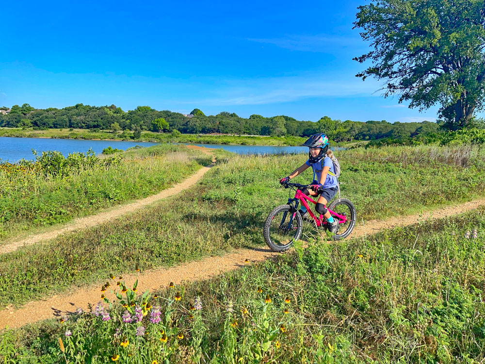 Little grom riding down singletrack trail by a lake on the Trailcraft Blue Sky 20