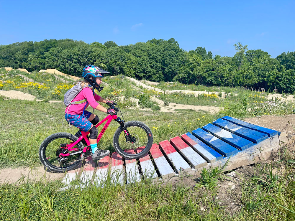 Rider on Trailcraft Blue Sky hardtail riding up a ramp painted like the flag of Texas.