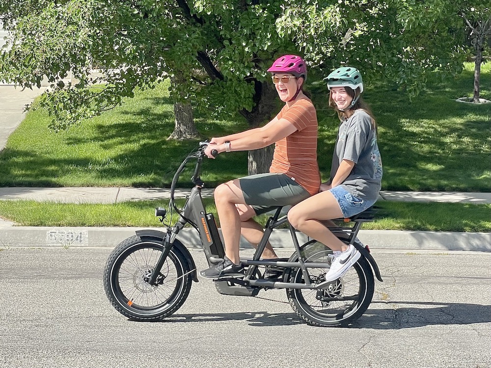 mom and daughter riding on the RadPower RadRunner 3 Plus utility ebike with the passenger kit and passenger bars