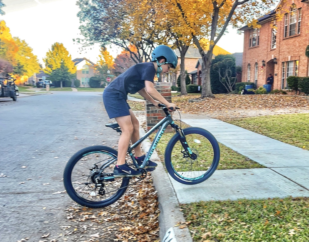 Boy jumping the curb on the Polygon Premier XC Disc 24" kids bike.