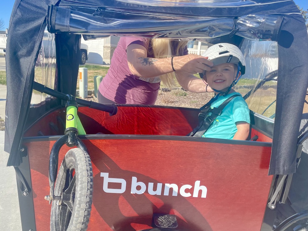 toddler sitting in the Bunch Bike while his mom adjusts his helmet