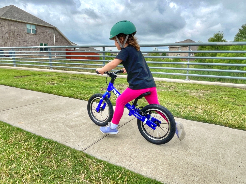 3 year old girl racing down sidewalk on Frog Tadpole Plus balance bike