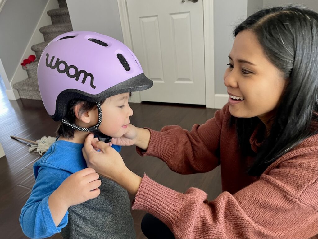 mom adjusting the chin strap length of the woom helmet on her son