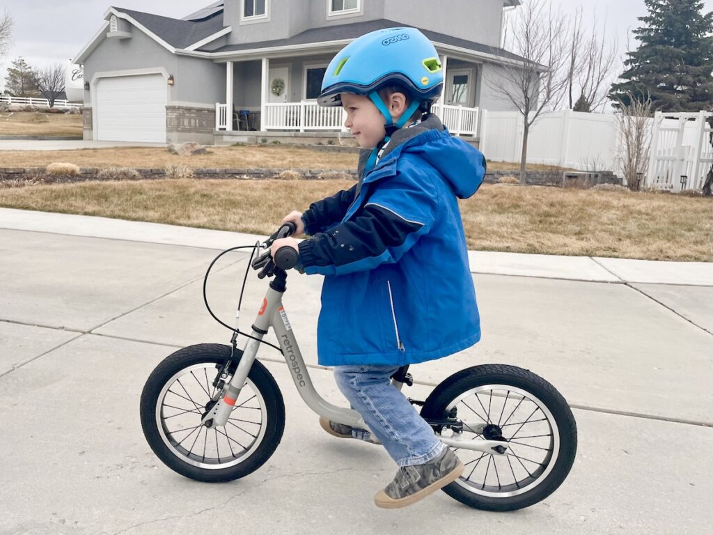toddler wearing the ozmo sidekick helmet while riding the Retrospec Cub Plus XL balance bike