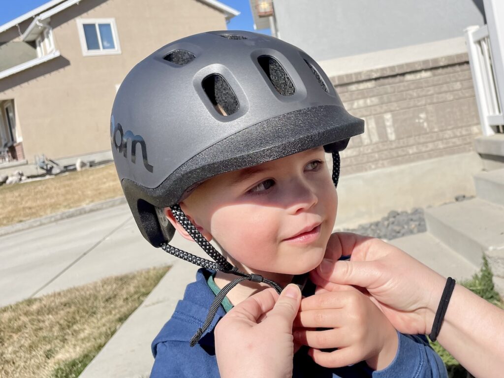 young child having the chin strap of the woom helmet adjusted