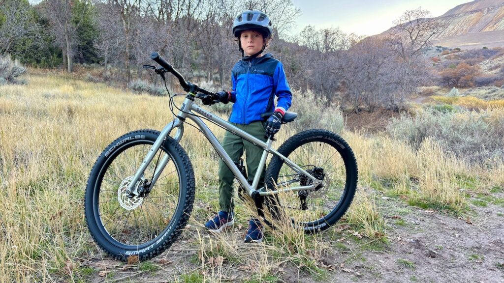 child standing by the early rider seeker 24 on a trail